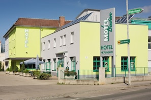 Un hotel con fachada verde, múltiples ventanas y un letrero que indica un aparcamiento.