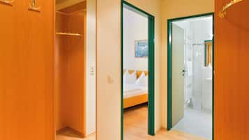 A hotel room with a wooden wardrobe, a bed with white bedding, and a green-framed door leading to a bathroom.