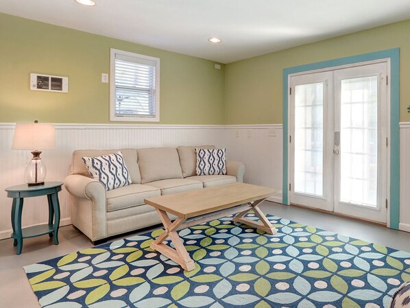 Un salon avec un canapé beige, une table basse en bois, une table d’appoint turquoise et un tapis à motifs.