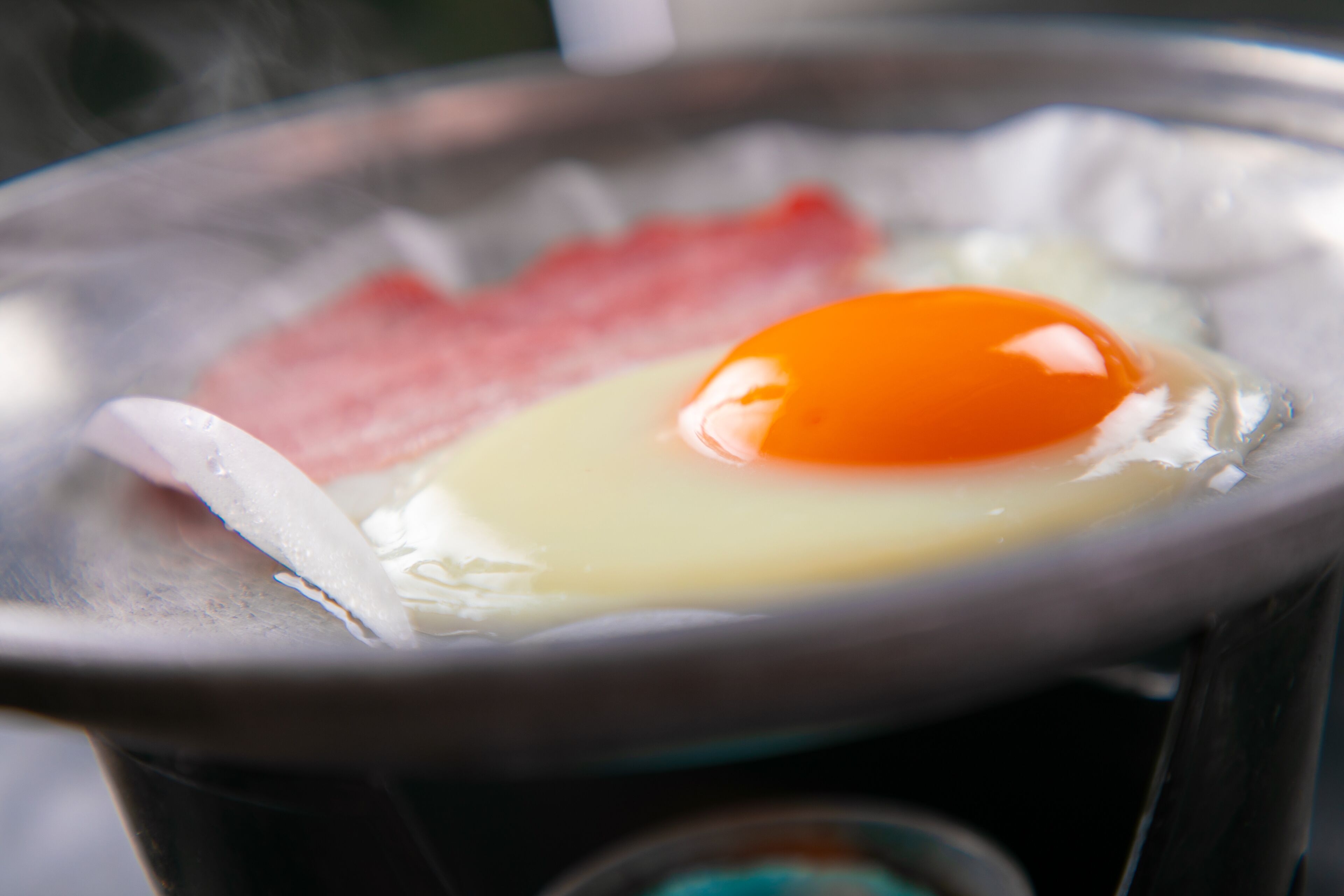 A close-up of a hot pot with a raw egg and slices of meat.