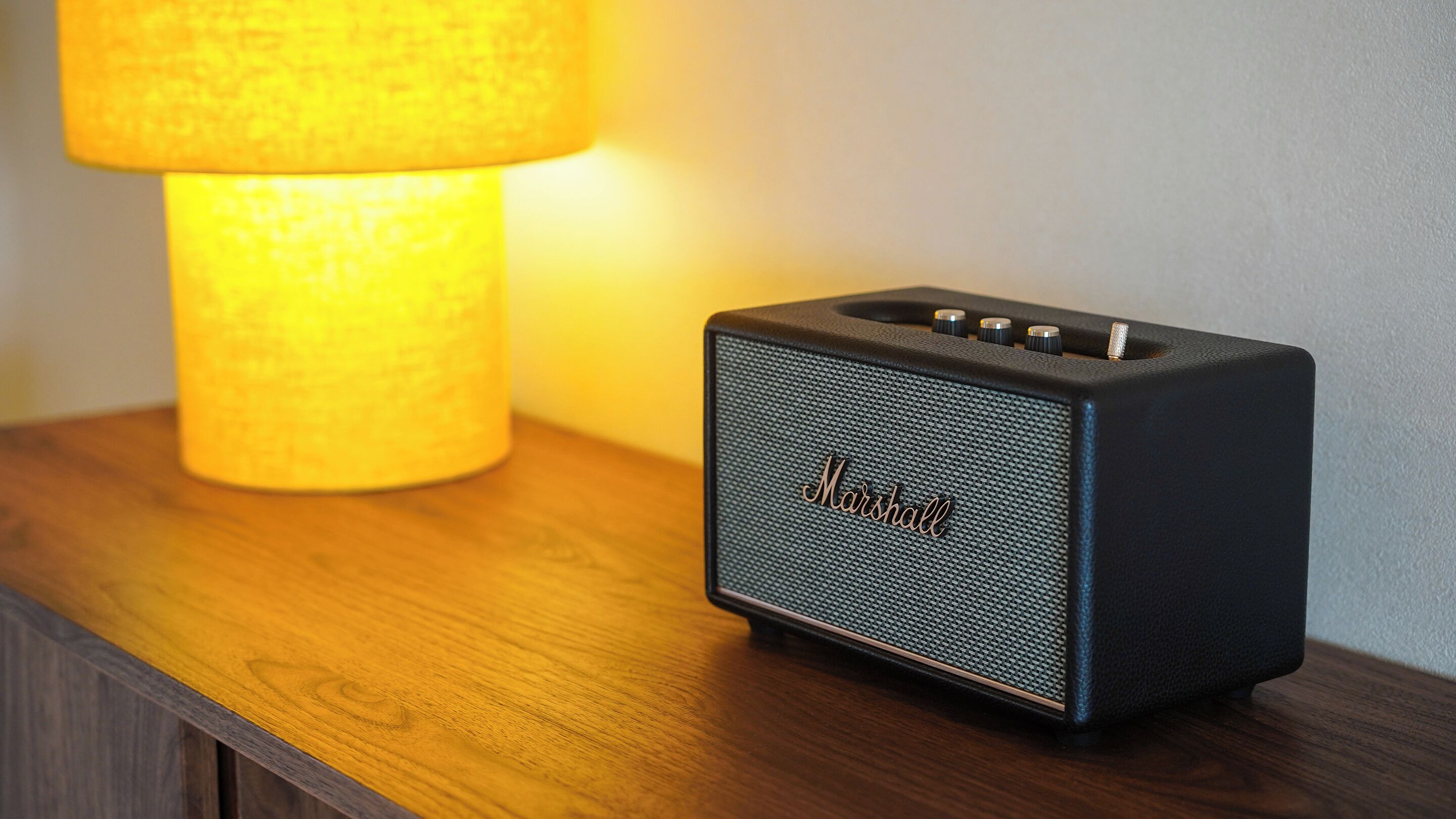 A black Marshall speaker on a wooden nightstand next to a lamp.