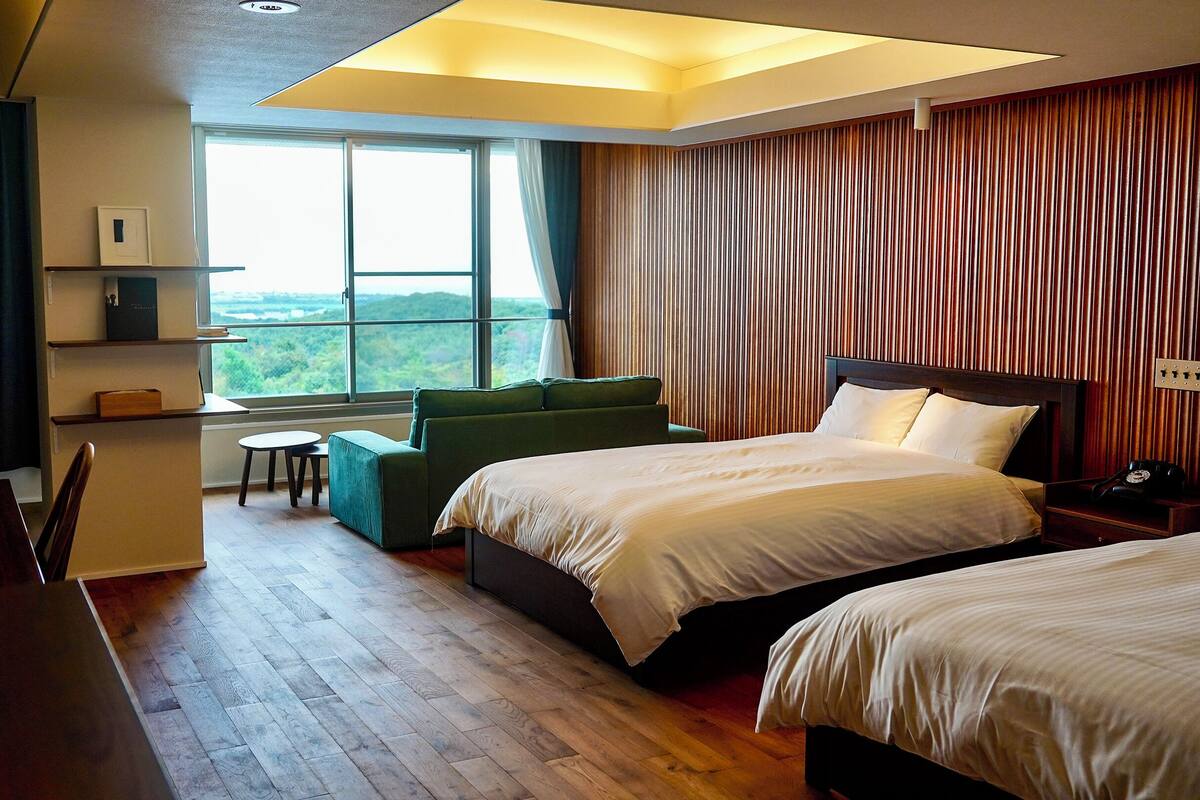 A hotel room with two beds, a sofa, a small table, and a view of the outdoors.