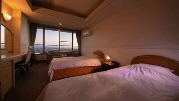A hotel room with two beds, a desk, a chair, and a large window offering a city view.