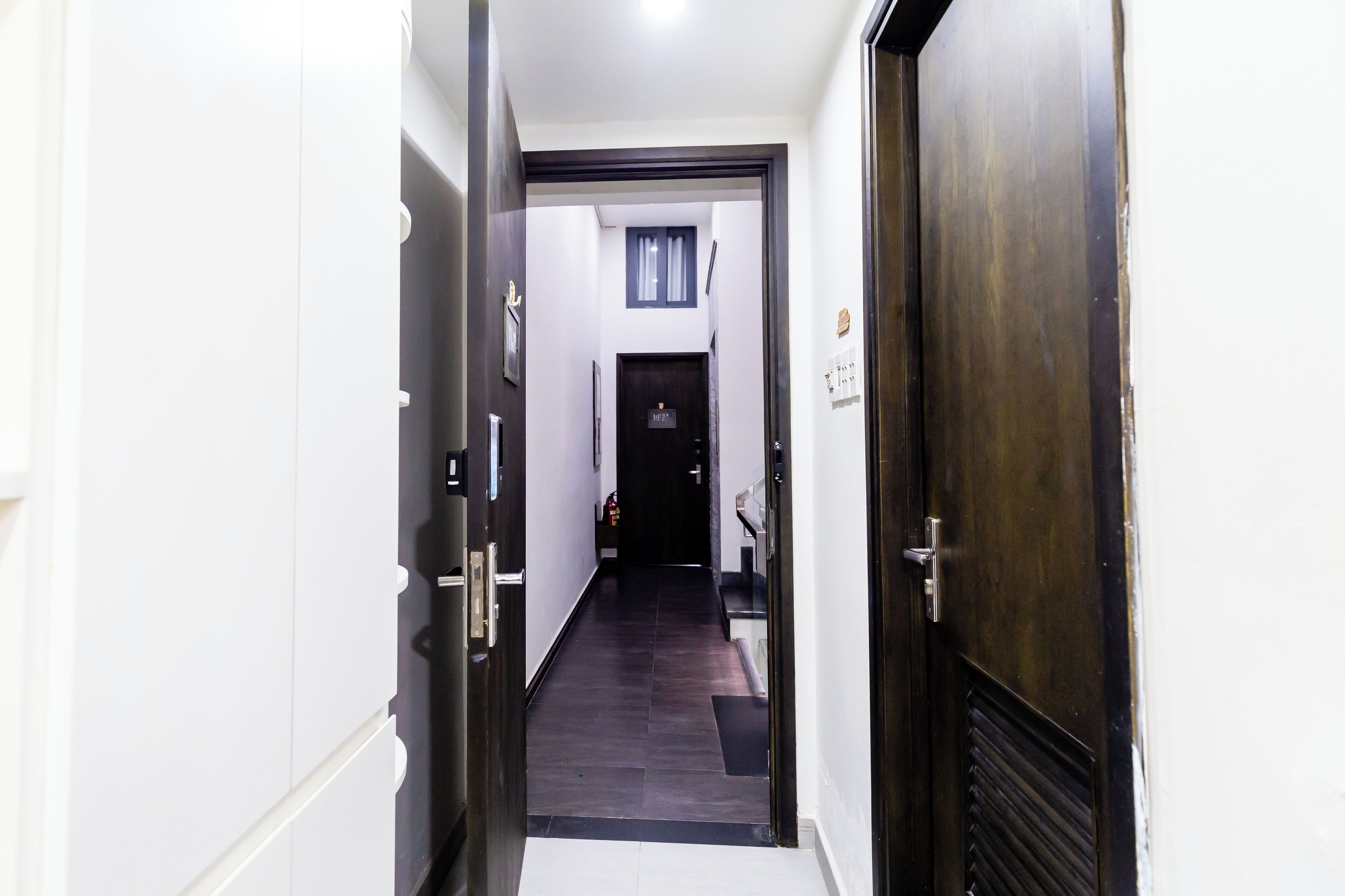A hallway with a dark wooden door on the right, a white door on the left, and a black door at the end.