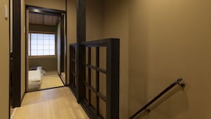 A hallway with wooden flooring, a dark ceiling, and a view into a room with a bed. - Shirakabanoyado-Uchikyuhoji (Osaka)