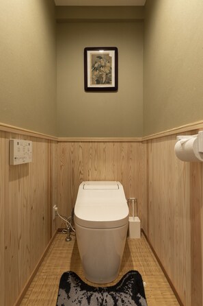 Une petite salle de bain aux murs lambrissés, avec des toilettes, un tableau encadré et un plancher en bois.