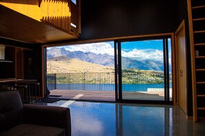 A modern interior with a large sliding glass door leading to a balcony with a mountain view. - Award Winning Architecturally Designed Pad (Queenstown)