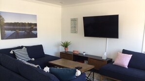 A living room with two dark blue sofas, a wooden coffee table, a flat-screen TV mounted on the wall, a potted plant, and a framed picture of a lake. - BALBOA ISLAND WATERFRONT .... STEPS TO THE SAND (Newport Beach)