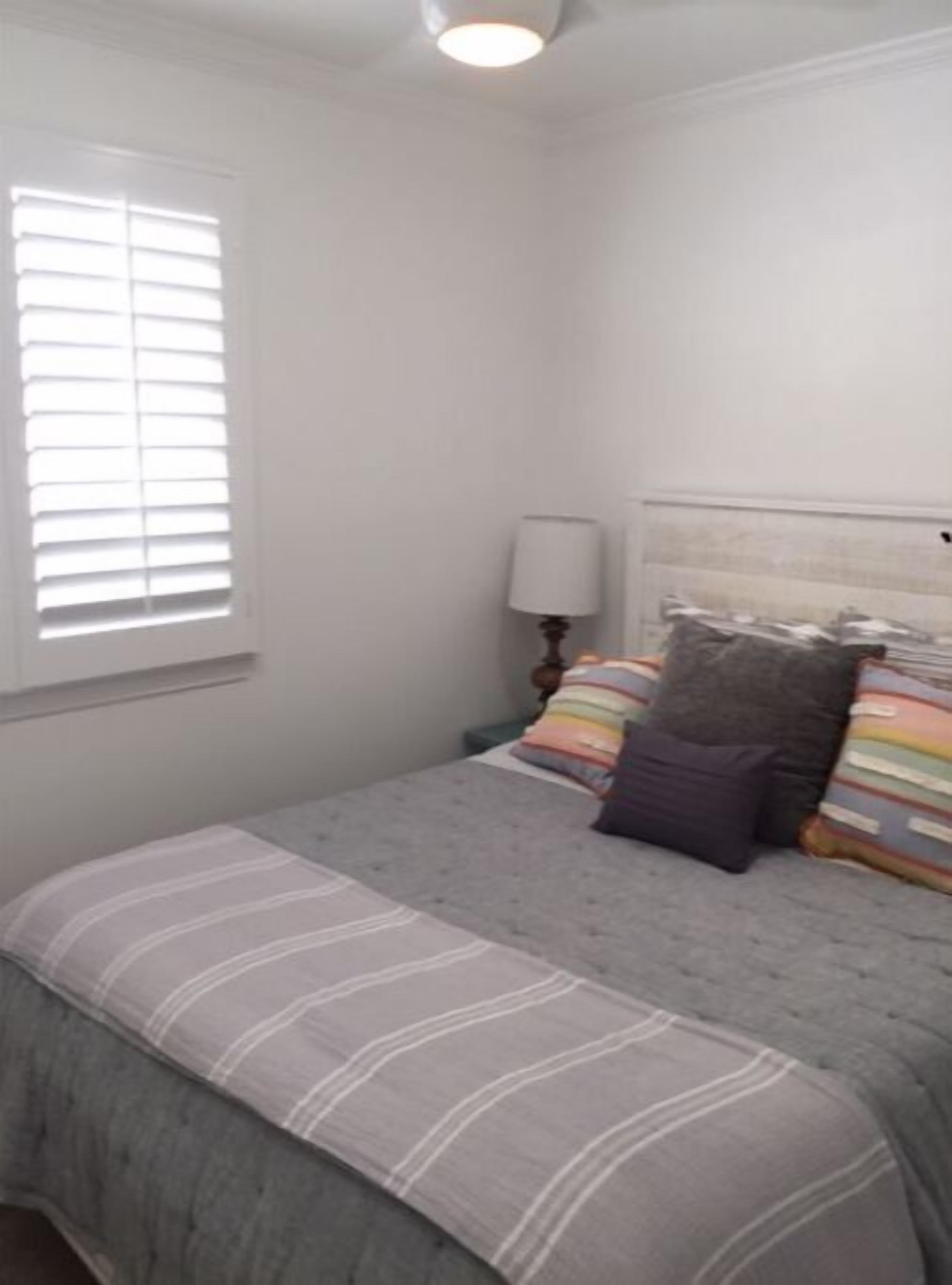 A bedroom with a bed, pillows, a nightstand, and a window with blinds.