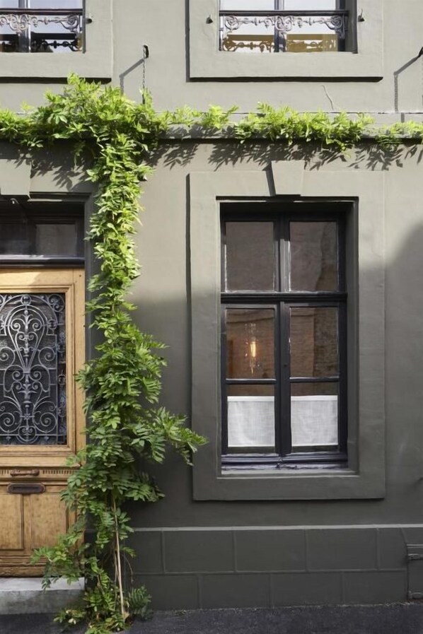 A building facade with a window, a door with a decorative metal grille, and a vine-covered wall. - PieuX (Montreuil-sur-Mer)