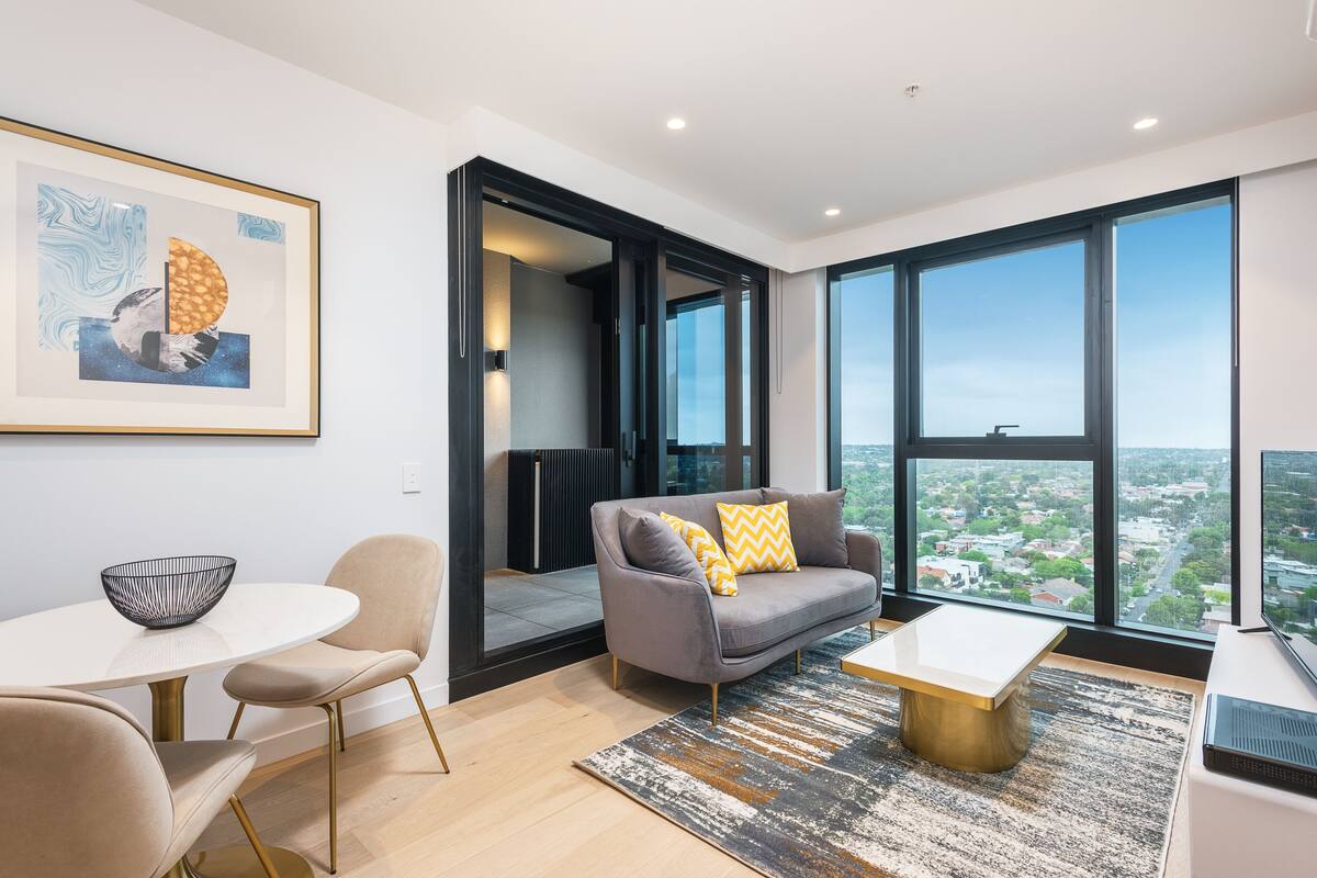 A modern living room with a grey sofa, a white coffee table, and a large window offering a city view.