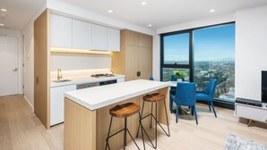 A modern kitchen with a white island, wooden accents, and a large window offering a city view. - Sky One Apartments by CLLIX (Box Hill)