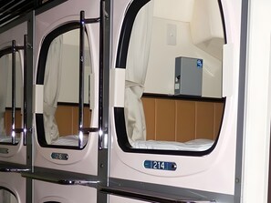 A train carriage with individual sleeping compartments, each with a window, a bed, and a small table. - Hotel Palms Tenmonkan (Kagoshima)