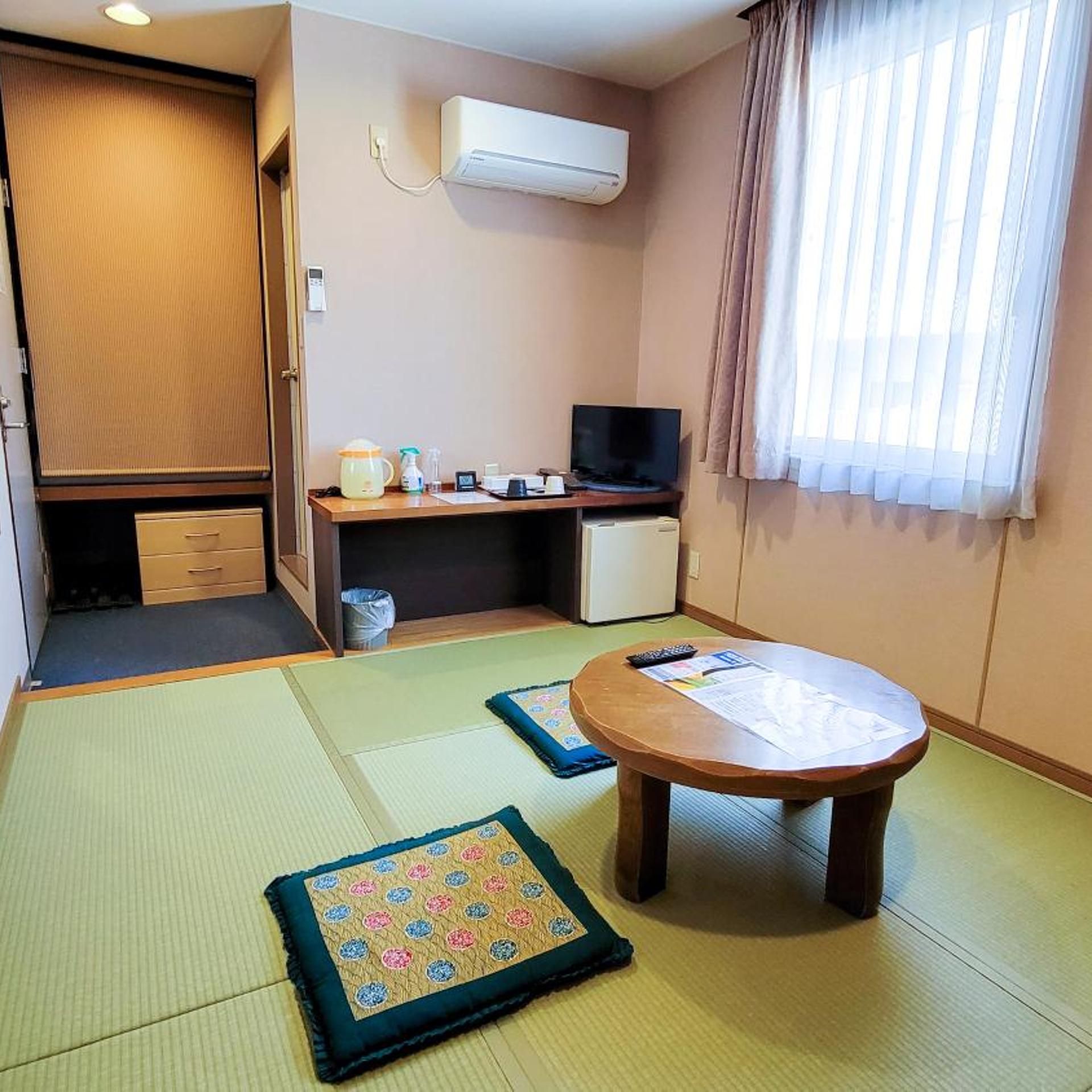 Habitación con esteras de tatami, una pequeña mesa, un televisor y un escritorio con una computadora.