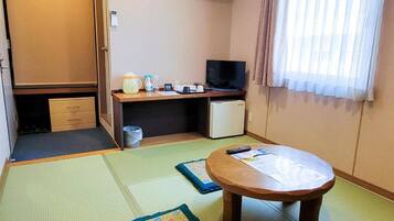 Habitación con esteras de tatami, una pequeña mesa, un televisor y un escritorio con una computadora.