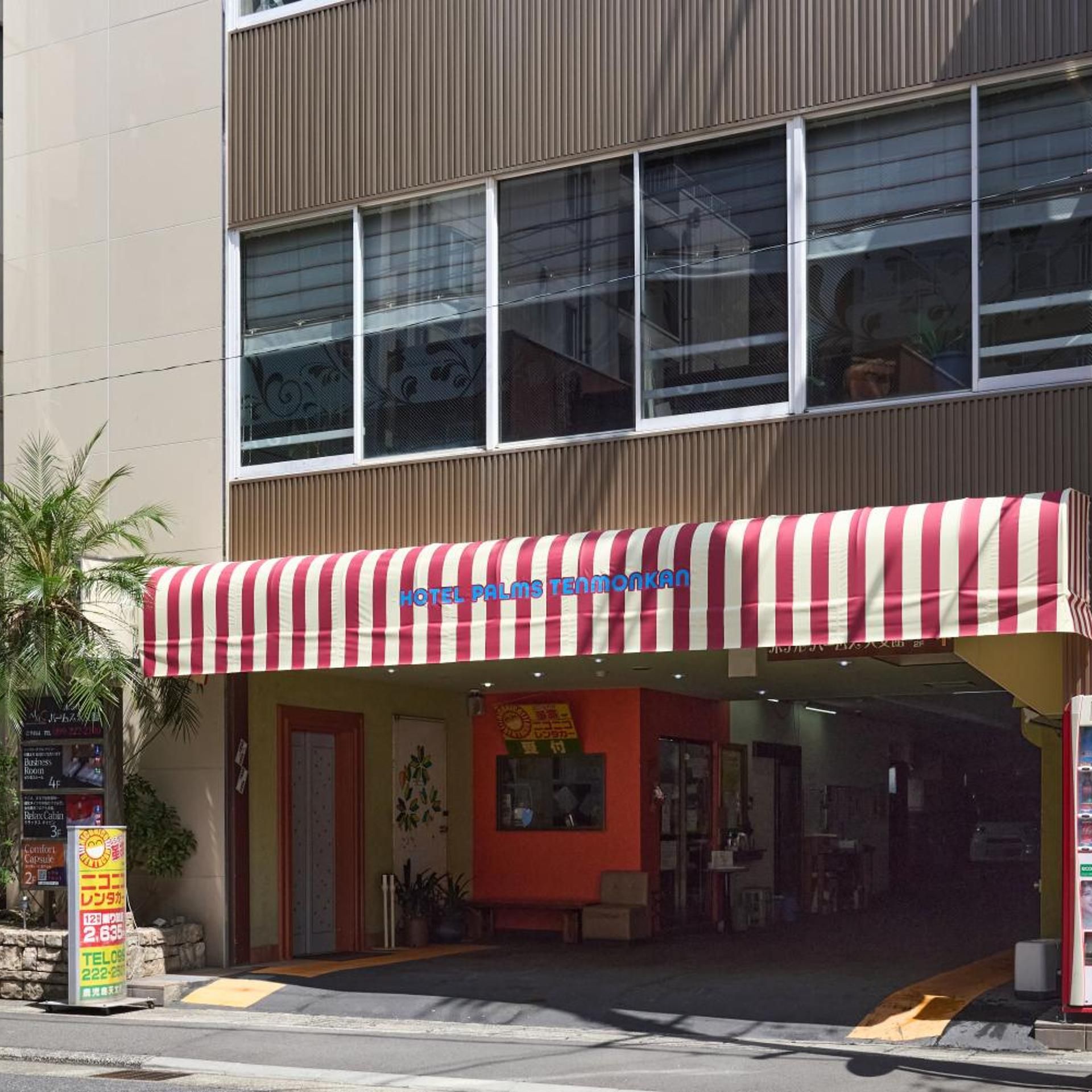 Hotel com toldo listrado em vermelho e branco, fachada vermelha e entrada visível.