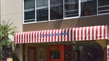 Hotel com toldo listrado em vermelho e branco, fachada vermelha e entrada visível.