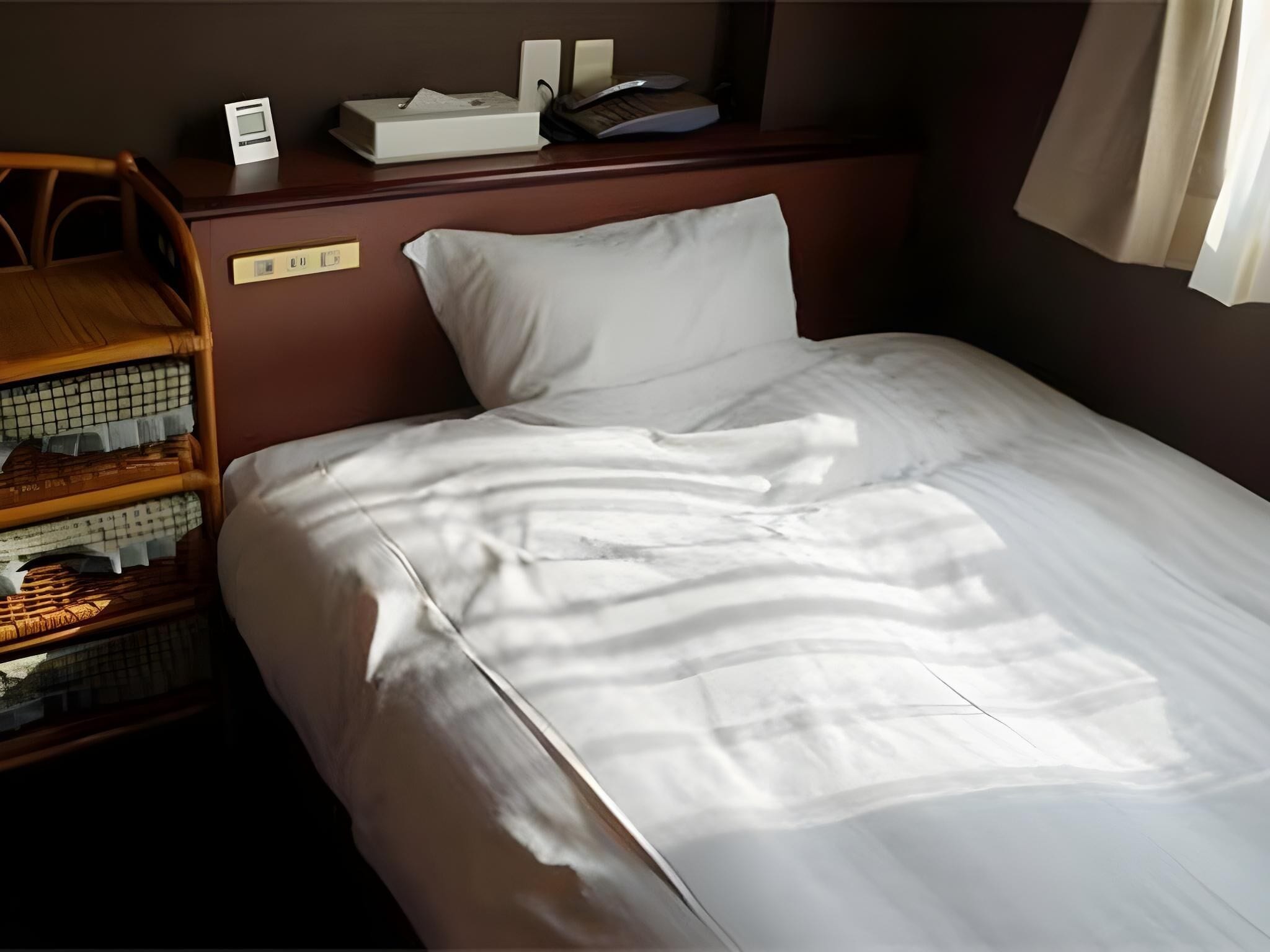Uma cama bem arrumada com lençóis brancos, cabeceira de madeira e uma pequena mesa de cabeceira com abajur e um livro.