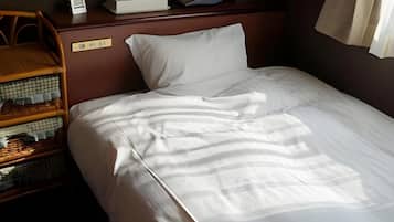 Uma cama bem arrumada com lençóis brancos, cabeceira de madeira e uma pequena mesa de cabeceira com abajur e um livro.