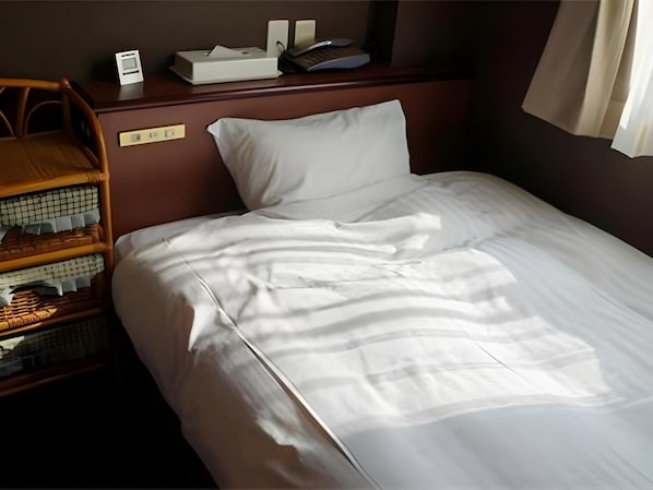 Una cama bien hecha con ropa de cama blanca, un cabecero de madera y una mesita de noche con una lámpara y un libro.