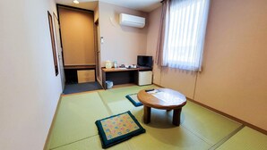 A compact hotel room with tatami mat flooring, a small wooden table, a television, and a kitchenette. - Hotel Palms Tenmonkan (Kagoshima)