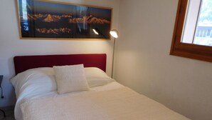 Een netjes opgemaakt bed met een rood hoofdeinde, een wit kussen en een witte deken.