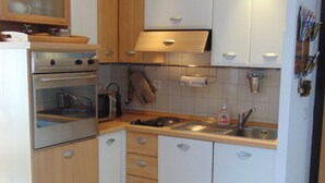 Een kleine keuken met houten keukenkastjes, een inbouwoven, een magnetron, een spoelbak en een kookplaat.