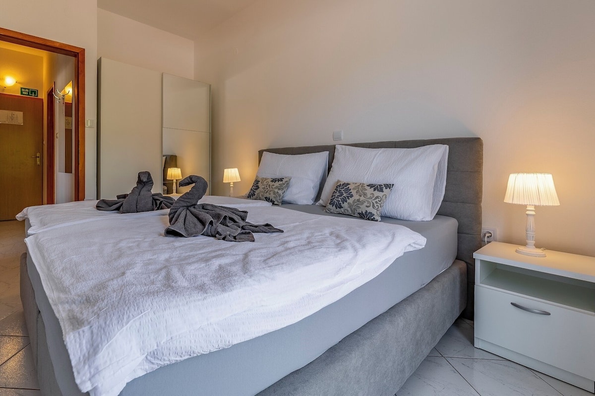 Ein Hotelzimmer mit einem großen Bett, einem Nachttisch mit Lampe und einer Tür mit Ausgangsschild.