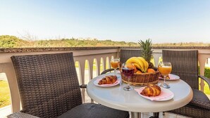 A table set with croissants, a fruit basket, and drinks on a balcony with wicker chairs and a view of the landscape. - Apartmani Rok (Medulin)