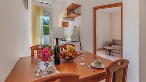 A dining area with a wooden table, chairs, a bowl of fruit, wine glasses, and a bottle of wine. - Apartmani Rok (Medulin)