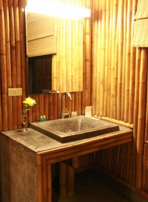 A bathroom with a bamboo wall, a sink, and a mirror. - Kirati Beach Resort (Koh Samui)