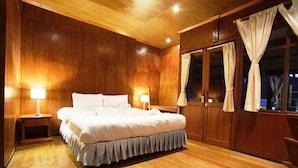 A wooden-paneled bedroom with a large bed, two bedside tables with lamps, and a window with curtains. - Kirati Beach Resort (Koh Samui)