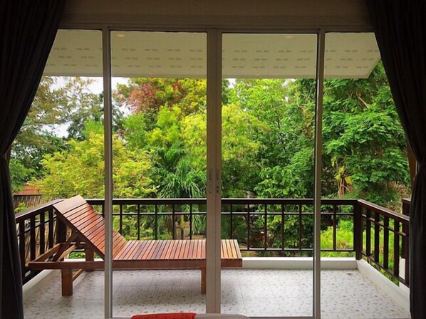 A balcony with a wooden bench, a glass door, and a view of lush greenery. - Kirati Beach Resort (Koh Samui)