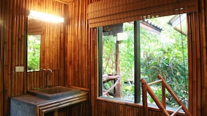 A bathroom with a wooden interior, a sink, and a window with a view of greenery. - Kirati Beach Resort (Koh Samui)