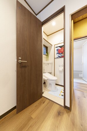 A wooden door leading to a bathroom with a toilet, a shower, and a towel rack.