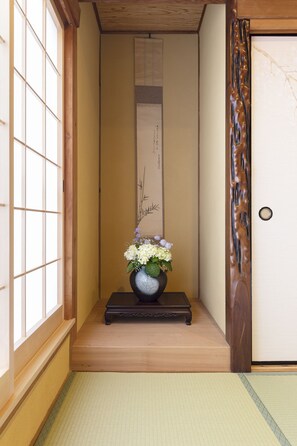Un intérieur japonais traditionnel avec un sol recouvert de tatamis, une porte en bois et un vase rempli de fleurs.