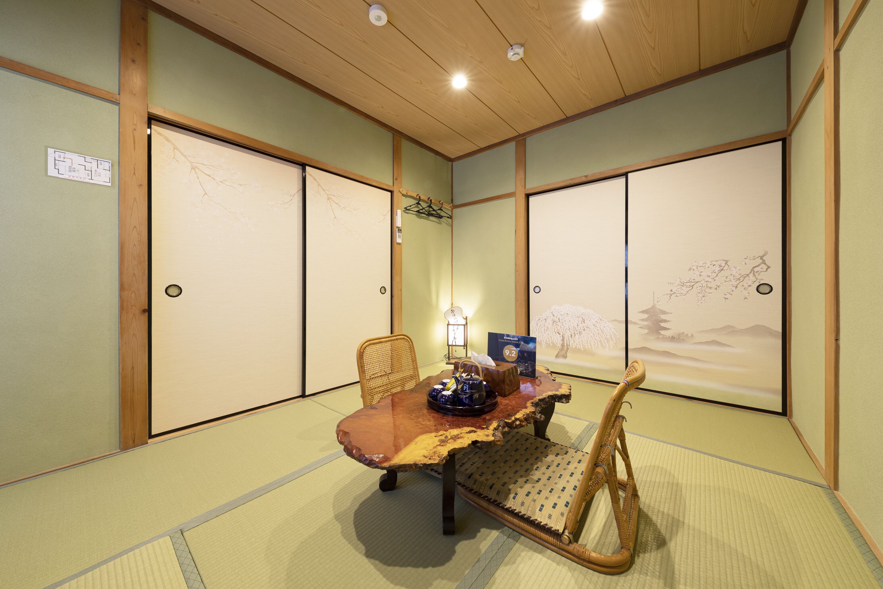 A traditional Japanese room with tatami flooring, a low wooden table, a chair, and sliding doors with artwork.