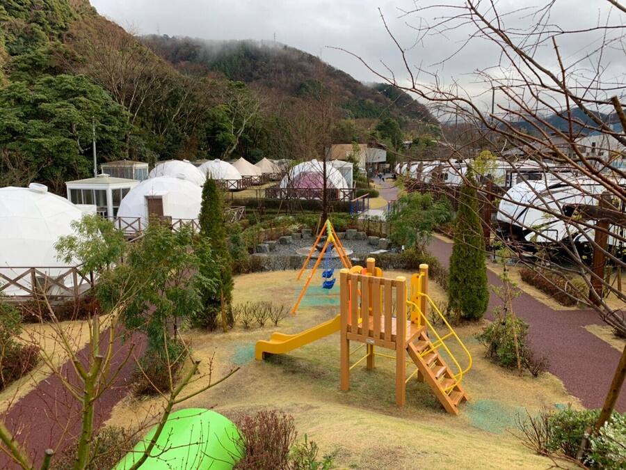Un parque infantil con tobogán y estructura para escalar, rodeado de tiendas de campaña y árboles.
