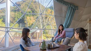 A cozy indoor seating area with a table, chairs, and a view of a forest through large windows. - Ufufu Village - Glamping (Izu)