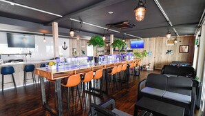 Zona de bar con una barra alargada, varios taburetes y un área de estar con sofás.