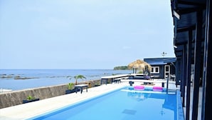 Una piscina con vista al mar, una estructura de techo de paja y un edificio con fachada oscura.