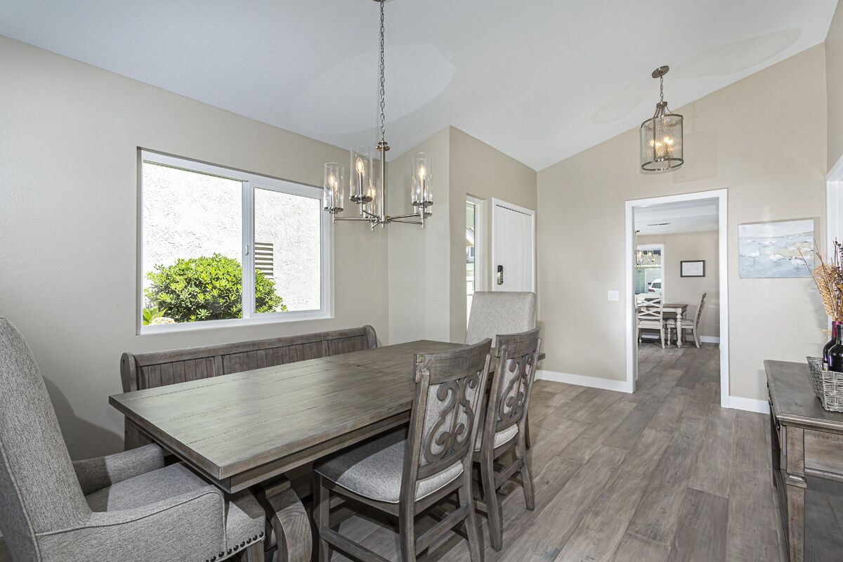 A dining area with a wooden table and chairs, a chandelier, and a view of greenery outside.