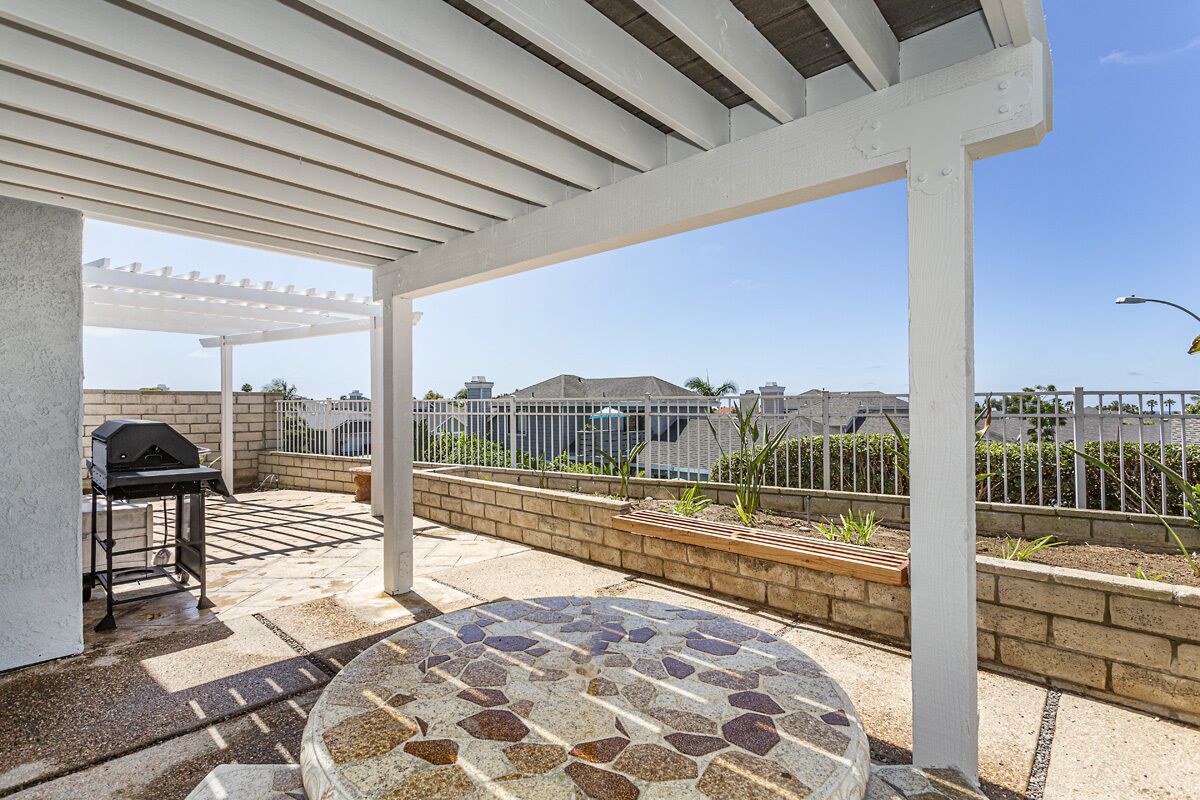 A covered patio area with a grill, a round stone table, and a view of the neighborhood.