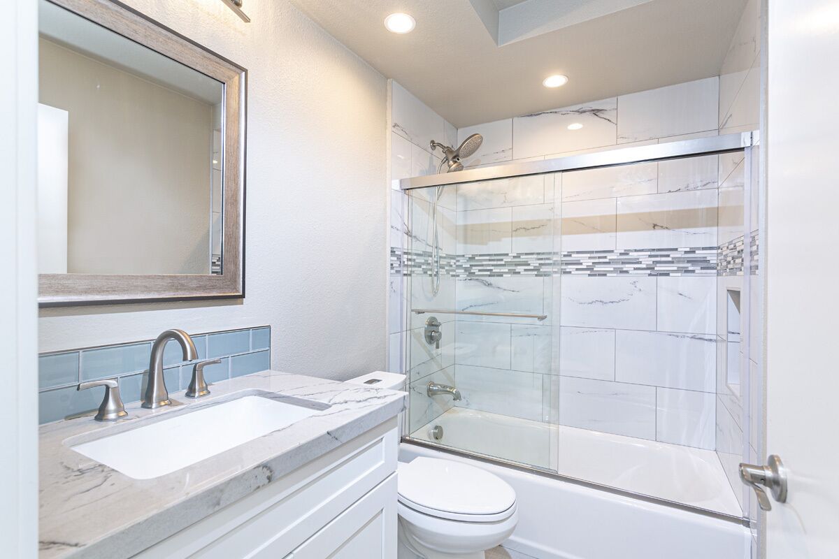 A modern bathroom with a glass-enclosed shower, a white sink with a marble countertop, and a large mirror above the sink.