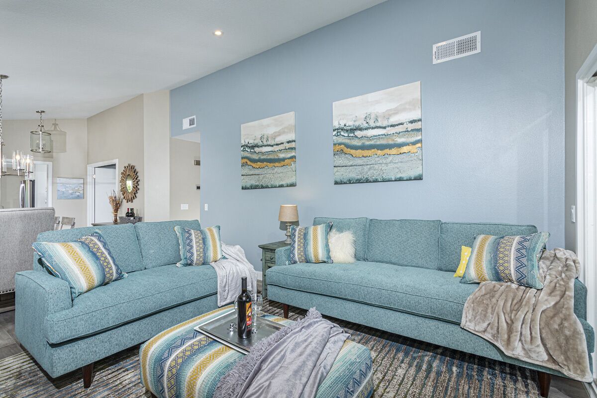A living room with a blue sofa set, a coffee table, and a patterned rug. There are wall art pieces and a chandelier.