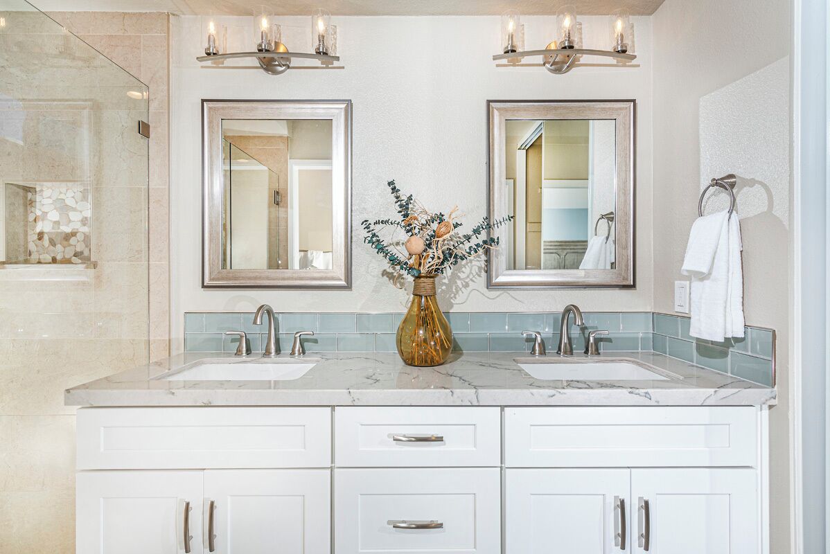 A bathroom with two sinks, a marble countertop, a vase with dried flowers, and two wall-mounted mirrors.