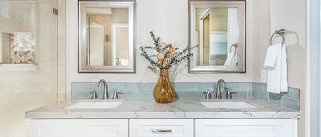 A bathroom with two sinks, a marble countertop, a vase with dried flowers, and two wall-mounted mirrors.