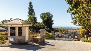 A gated entrance with a small pavilion, paved walkway, and a view of the ocean and residential area.