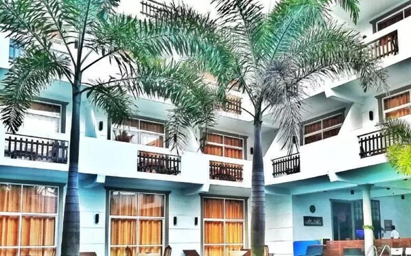 A multi-story building with balconies, large windows, and palm trees. - Nil diya mankada safari lodge (Udawalawa)