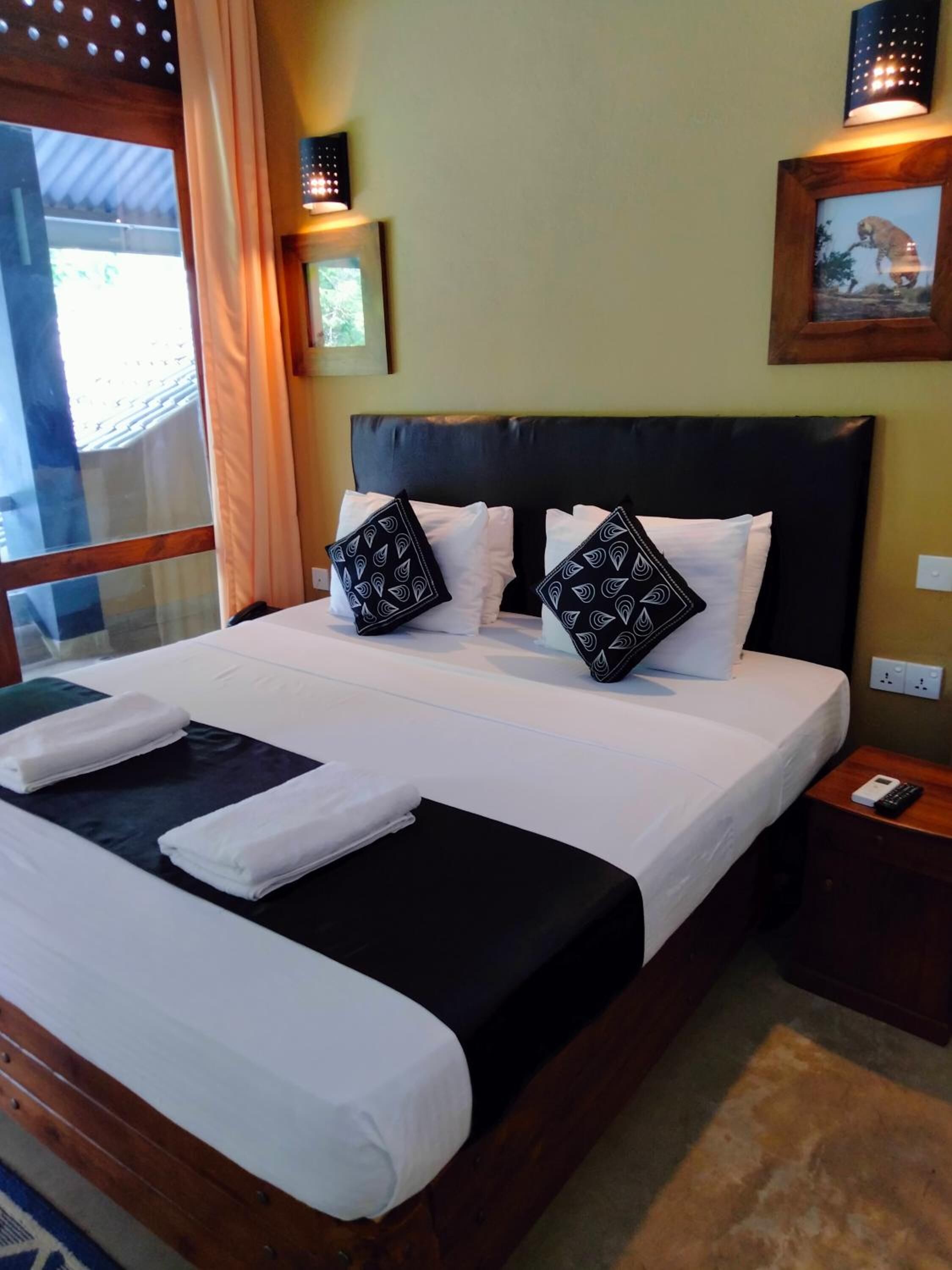 A neatly made bed with white linens and black pillows, a wooden headboard, and a nightstand with a remote control.